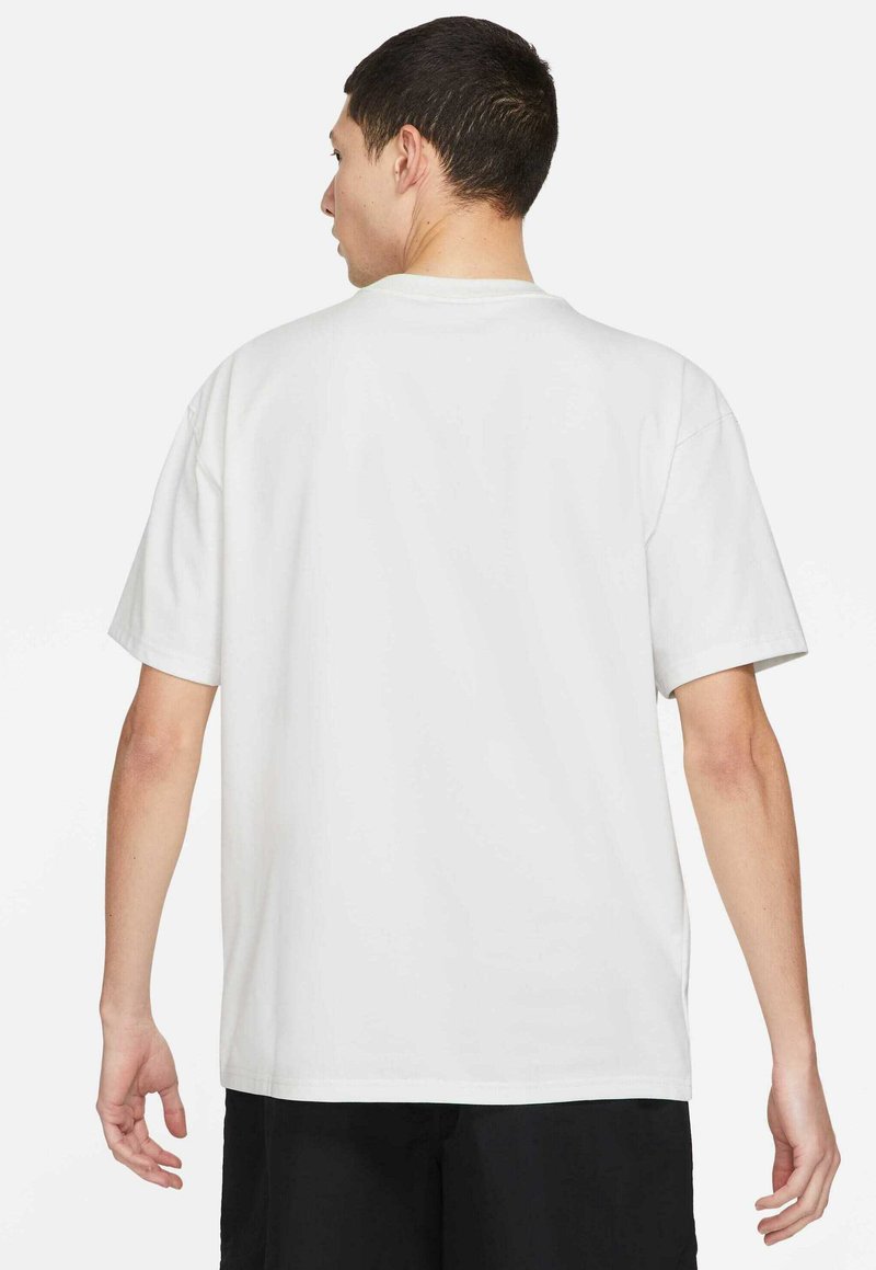 Homme de dos portant un t-shirt blanc uni à manches courtes et un short noir sur un fond blanc.
