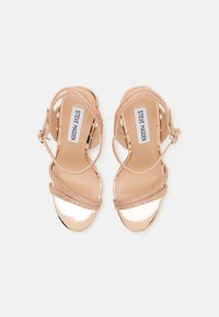 Sandalias de tacón alto con tiras en metálico rosa dorado, con tiras trenzadas adornadas con strass y cierre de hebilla en el tobillo.
