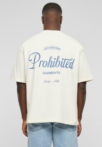 Cream cotton t-shirt featuring large blue text that reads "Prohibited Garments" with a decorative leaf accent, styled in a relaxed fit.