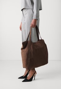 Borsa a spalla in suede marrone con texture morbida, design spazioso e manici lunghi, abbinata a scarpe con tacco nere.