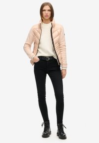 Lys pink quiltet jakke med sort lynlås, cremet sweater, sorte skinny jeans og sorte snørebånd støvler. Glat overflade og tætsiddende design.