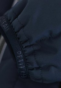 Manica di giacca blu navy con polsino arricciato e fascia elastica testurizzata. Il materiale è liscio con una leggera lucentezza e dettagli cuciti.