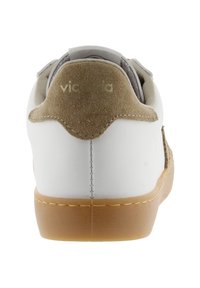 Sneaker blanc avec un talon en suede marron clair et une semelle en gomme, vu de l'arrière, présentant des détails cousus et un texte de logo sur le talon.