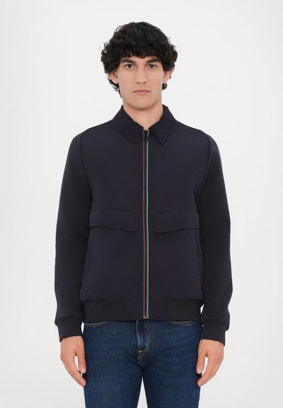 Veste zippée bleu marine avec un col, deux poches avant et une fermeture éclair multicolore. Fabriquée en tissu texturé, elle présente des poignets et un ourlet côtes.