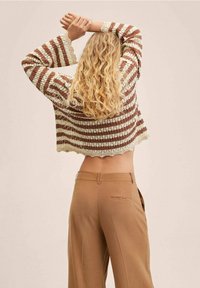 Häkelpullover in Creme- und Brauntönen, gekürztes Design mit gewelltem Saum; kombiniert mit beigefarbenen, weiten Hosen mit einer rückseitigen Tasche.