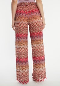 Pantalons larges en tissu à motifs zigzag multicolores, avec des tons rouges, orange, bleus et blancs, dotés d'un ourlet fringé.