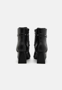 Black heeled ankle boots made of smooth faux leather, featuring a decorative strap with studs and a side zipper for easy wear.