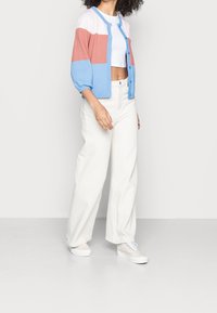 Knit cardigan in blue, pink, and white, features a round neckline, button front, and puffed sleeves. Paired with white wide-leg pants and sneakers.