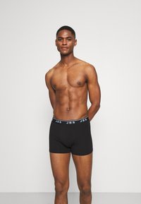 Svarta boxerkalsonger med en figursydd design och elastisk midja med "JBS"-logotyp i kontrasterande vitt. Bomullsmaterial, slät textur.