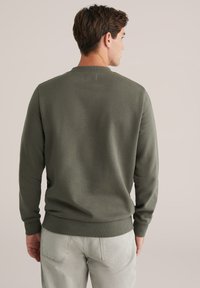 Donkergroen sweatshirt met ribbelkraag en -manchetten, gemaakt van zachte stof. De achterkant is eenvoudig met een relaxte pasvorm, gecombineerd met lichtgrijze broek.
