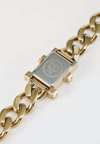 Orologio da polso dorato con quadrante rettangolare argentato, cinturino a maglie, corona sul lato e logo del marchio ben visibile sul retro.