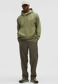 Hoodie vert olive avec une poche avant, associé à un pantalon cargo olive avec poches latérales et des chaussures de randonnée marron.