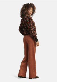 Zwarte sweater met roestkleurig luipaardprint, ballonmouwen; gecombineerd met roestkleurige wijde broek van zacht stof; model kijkt naar rechts.