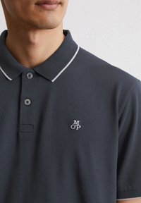 Dark blue polo shirt made of cotton, featuring a white collar trim, three buttons, and a small embroidered "MOP" logo on the chest.