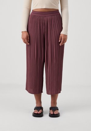 Plissé culottes in donker bordeaux met een getextureerde tailleband. Korte lengte, vloeiende stof en een losse pasvorm. Gecombineerd met zwarte sandalen.