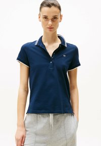 Granatowa koszulka polo wykonana z bawełny, posiadająca kołnierzyk z białym wykończeniem i krótkie rękawy. Zawiera małe logo na piersi.