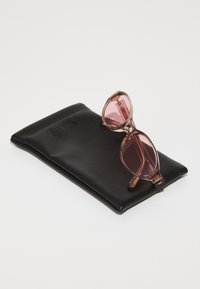 Lunettes de soleil teintées de rose avec un design angulaire, monture transparente et un étui en cuir noir embossé avec "QUAY".