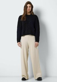 Zwarte harige trui met lange mouwen, gecombineerd met beige wijde broek en zwarte schoenen. Eenvoudig ontwerp met een gestructureerde afwerking.