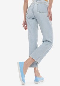 Zapatos azul claro sin cordones hechos de un material suave con una suela de goma blanca. Presentan una parte trasera texturizada con acentos de logo. Combinados con denim claro.