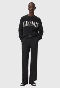 Juodas megztukas su "ALLSAINTS" logotipu baltu raštu, derinamas su juodomis kelnėmis. Tekstūruota medžiaga, laisvas siluetas ir paprastas dizainas. Juodi batai.