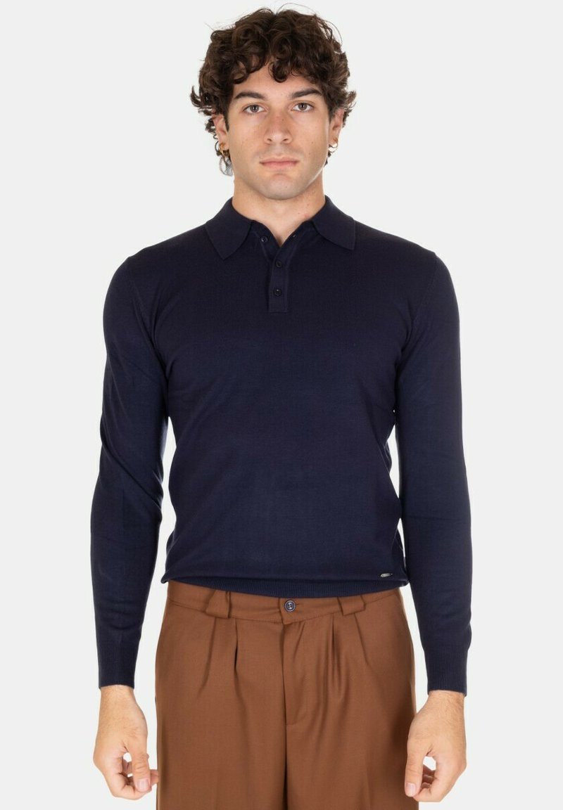 Polo a maniche lunghe di colore blu navy con colletto, patta per bottoni e polsini a coste. Abbinato a pantaloni con pieghe marroni.