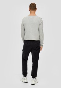 Szary longsleeve, czarne spodnie cargo z kieszeniami oraz białe trampki z przezroczystymi akcentami. Gładka faktura, luźny krój.