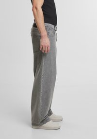 Jeans en denim gris à coupe ample, présentant un design classique et cinq poches, portés avec des baskets blanches.