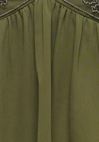 Olive green fabric with gathered pleats under a beaded trim, creating texture and decorative detail.