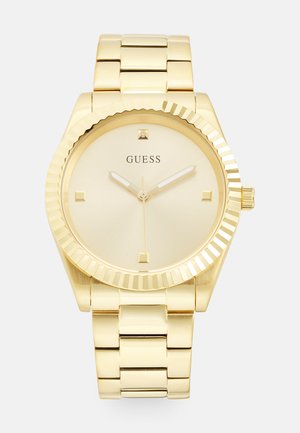 Montre-bracelet dorée avec un cadran rond, des marqueurs minimalistes et une lunette striée ; elle est dotée d'un bracelet à maillons qui complète son design.