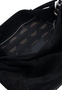 Wnętrze czarnej torebki zamszowej z kieszenią na zamek, wyłożone tkaniną o teksturze z powtarzającym się złotym logo "VENEZIA".