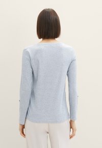 Camisa de manga larga de color azul claro, hecha de tejido de punto, con un patrón texturizado a rayas. Presenta un escote de tipo barco y ligeras aberturas laterales en el dobladillo.