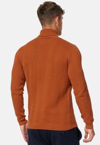 Pull à texture brun rouille mettant en avant un motif en chevrons, un col montant et des poignets et un ourlet côtelés. Le design présente une silhouette ajustée.