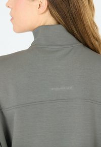 Grijze sporttop met een hoge kraag, een gladde textuur, platte naden en een subtiele logo-detail aan de achterkant.