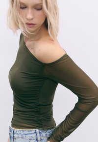 Olivengrøn tætsiddende top med én off-the-shoulder-design, gennemsigtige lange ærmer og samlede detaljer på siden.