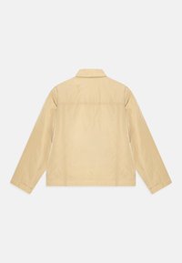 Ljusbeige jacka gjord av ett slätt, lätt material. Har krage, långa ärmar och en enkel, stilren design utan synlig hårdvara.