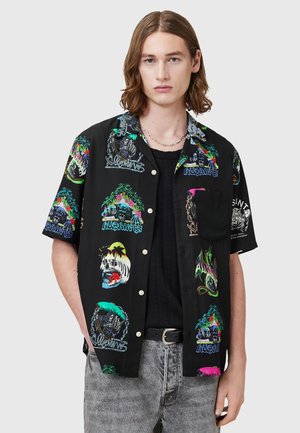 Camicetta nera a maniche corte con stampe grafiche colorate, inclusi teschi e design tropicali. Presenta una chiusura con bottoni e una tasca sul petto.