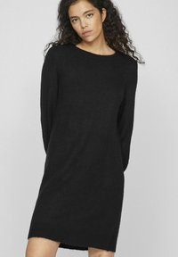 Abito maglione nero realizzato in materiale morbido, con scollo rotondo, maniche lunghe e vestibilità ampia con orlo leggermente asimmetrico.