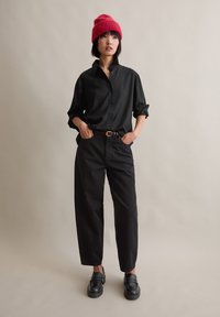 Svart knapp-up skjorte med rullede ermer, kombinert med svarte smale bukser og svarte loafers; accessorized med en rosa strikket lue.