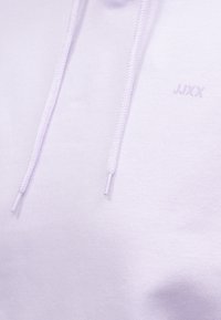 Hele lilla kapuutsärk, mis on valmistatud pehmest kangast. Omab reguleeritavaid nööre ja diskreetset logosid esiküljel. Sujuv tekstuur ja juhuslik disain.