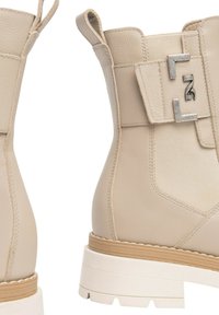 Stivaletti beige alla caviglia con finitura in pelle texturizzata, dotati di un dettaglio con fibbia laterale e una robusta suola bianca con accento tannato.