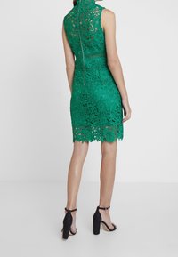 Robe en dentelle verte avec un motif floral, sans manches, col haut et ourlet festonné. Comprend une fermeture éclair au dos et une silhouette ajustée.