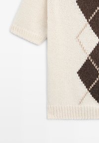 Gebreide trui met korte mouwen in crèmekleur, met een bruin-beige ruitpatroon aan de voorkant.