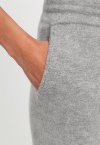 Grijze gebreide kleding met een zijzak. De textuur is zacht en glad, met een getailleerd ontwerp en een nette afwerking aan de randen.