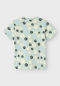 Camiseta de manga corta para niño pequeño en verde claro con un patrón de huellas en negro, blanco y azul en toda la tela.