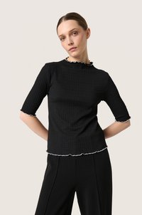 Sort tekstureret top med korte ærmer, der har en bølget hvid kant langs kraven og nederkanten. Tæt siddende design.