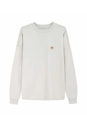 Bluza z długim rękawem w jasnobeżowym kolorze z okrągłym dekoltem, z małym brązowym logo słońca i fali na lewej piersi oraz ściągaczami przy mankietach.