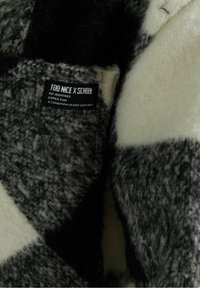 Grå och vit fleecejacka med ett strukturerat mönster, med en tät väv och en etikett som säger "TOO NICE X SCHOOL."