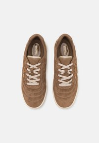 Sneaker in suede marrone con dettagli cuciti, lacci crema e un logo dorato di lato. Texture morbida e design con punta tondeggiante.