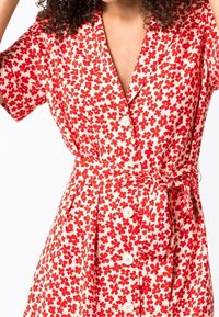 Czerwona sukienka w kwiatowy wzór z krótkimi rękawami, z przodu na guziki oraz z materiałowym paskiem w talii. Wykonana z lekkiego materiału, o luźnym kroju.