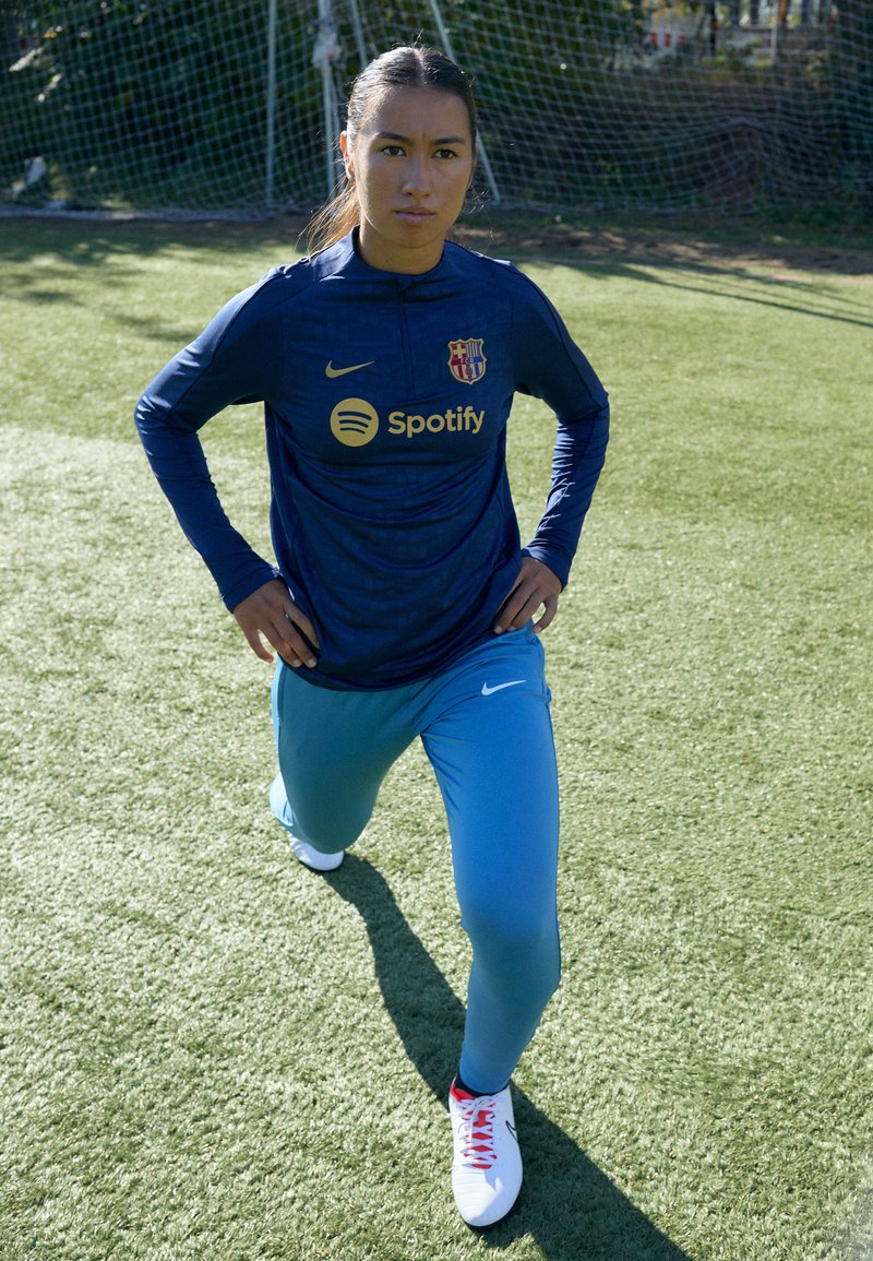 Blaues langärmliges Trikot mit einem Logo und Spotify-Branding, kombiniert mit hellblauen Sporthosen und weißen Schuhen mit roten Akzenten.